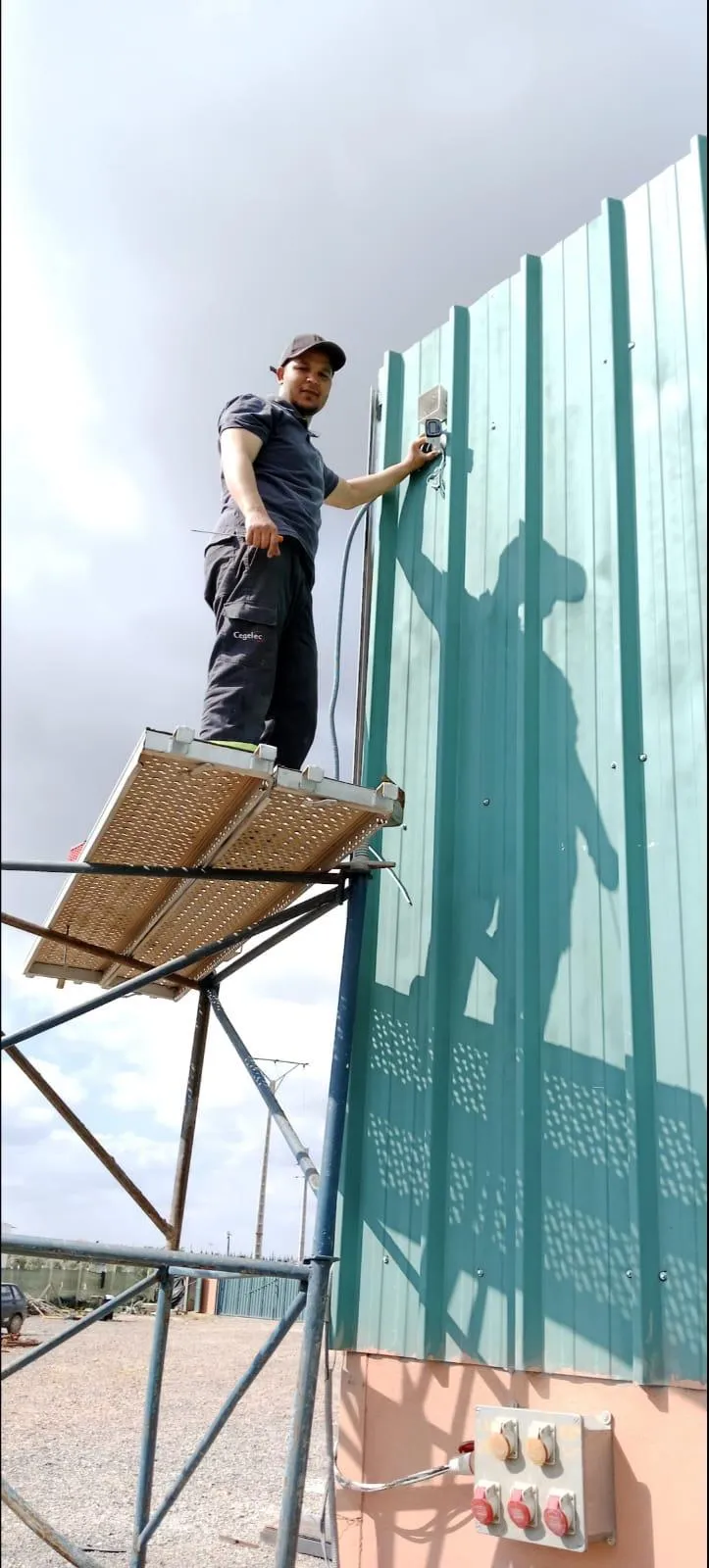 Électricien installant un équipement sur bardage métallique en hauteur